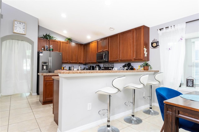 kitchen with lofted ceiling, kitchen peninsula, tasteful backsplash, appliances with stainless steel finishes, and a breakfast bar