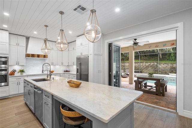 kitchen featuring pendant lighting, stainless steel appliances, white cabinets, and light hardwood / wood-style flooring