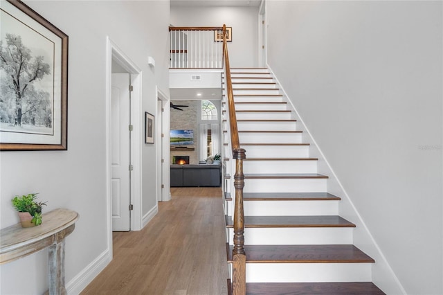 staircase with a large fireplace, ceiling fan, and hardwood / wood-style flooring