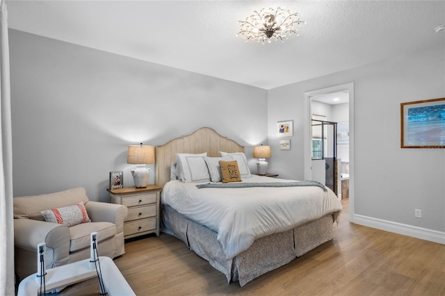 bedroom featuring a textured ceiling, light hardwood / wood-style floors, ensuite bath, and a notable chandelier