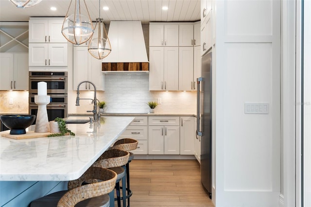 kitchen featuring white cabinets, light stone counters, a kitchen breakfast bar, stainless steel appliances, and premium range hood