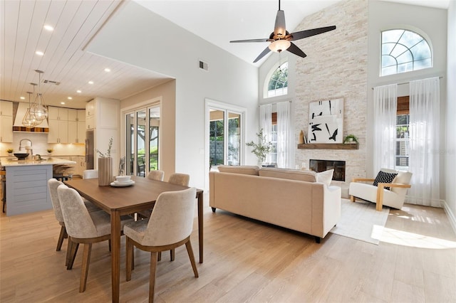 dining room featuring light wood-type flooring, a fireplace, a towering ceiling, and recessed lighting