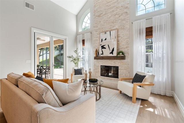 living room with baseboards, visible vents, wood finished floors, a stone fireplace, and high vaulted ceiling