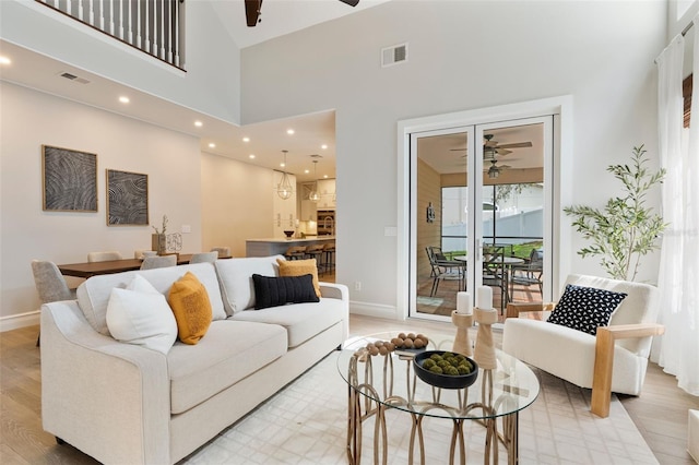 living room featuring a ceiling fan, light wood-type flooring, visible vents, and a high ceiling