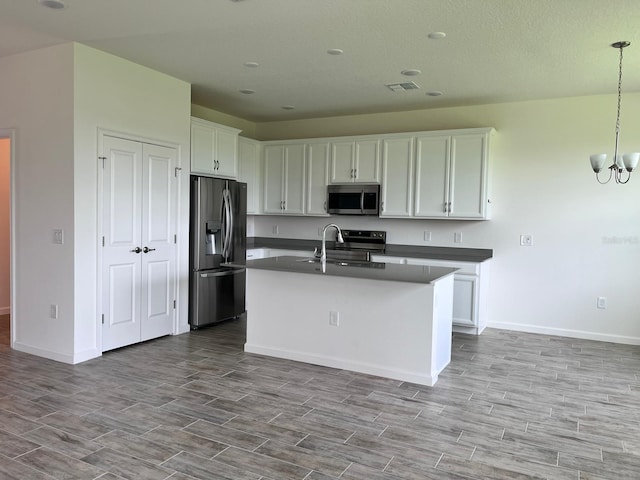 kitchen with a chandelier, pendant lighting, a center island with sink, stainless steel appliances, and white cabinets