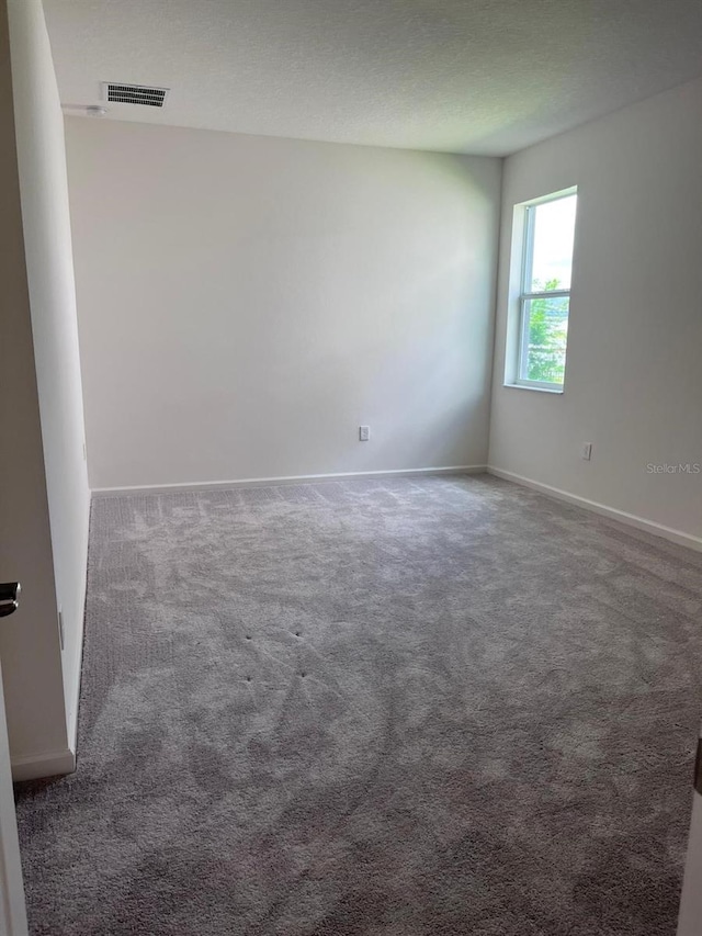 spare room featuring dark carpet and a textured ceiling