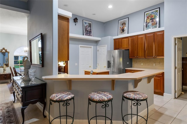 kitchen with a breakfast bar, kitchen peninsula, light tile patterned floors, and stainless steel fridge with ice dispenser