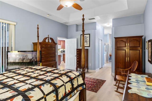 bedroom with a raised ceiling, light hardwood / wood-style floors, ensuite bath, and ceiling fan