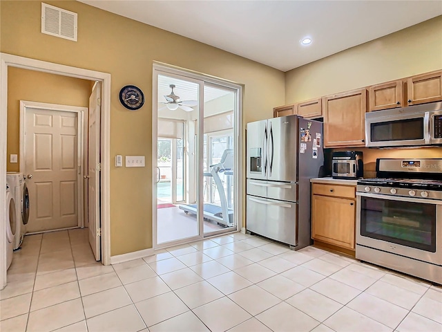 kitchen featuring light tile patterned floors, stainless steel appliances, ceiling fan, and washer and dryer