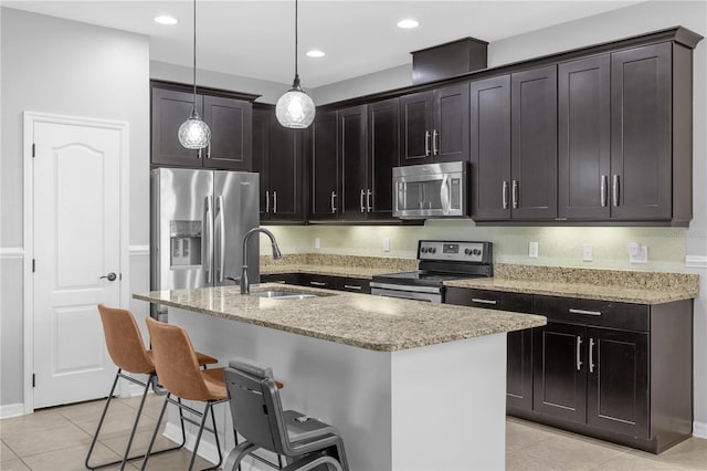 kitchen featuring light stone counters, sink, hanging light fixtures, stainless steel appliances, and a center island with sink