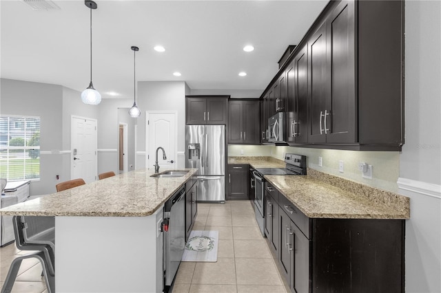 kitchen with a breakfast bar, a kitchen island with sink, sink, stainless steel appliances, and decorative light fixtures