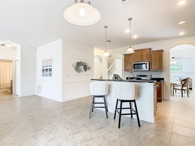 8920 Dove Valley Way, Davenport, FL 33896 - kitchen with stainless steel microwave, arched walkways, dark countertops, a breakfast bar area, and light tile patterned flooring