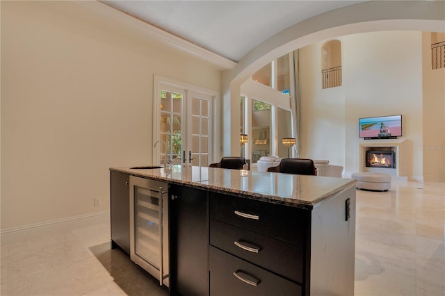 kitchen with sink, wine cooler, light stone countertops, ornamental molding, and a kitchen island