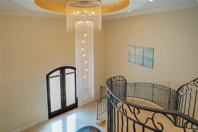 interior space with a tray ceiling, french doors, a chandelier, and ornamental molding