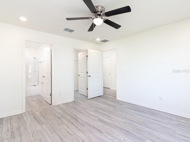 unfurnished bedroom with ensuite bathroom, a spacious closet, ceiling fan, and light hardwood / wood-style flooring