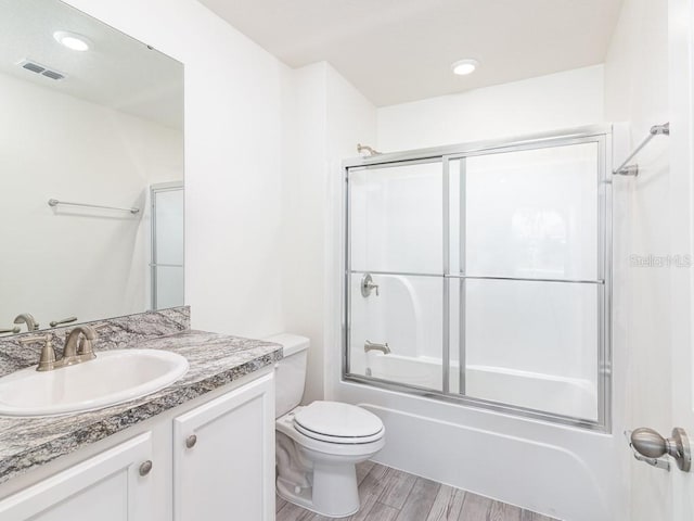 full bathroom featuring bath / shower combo with glass door, hardwood / wood-style flooring, vanity, and toilet