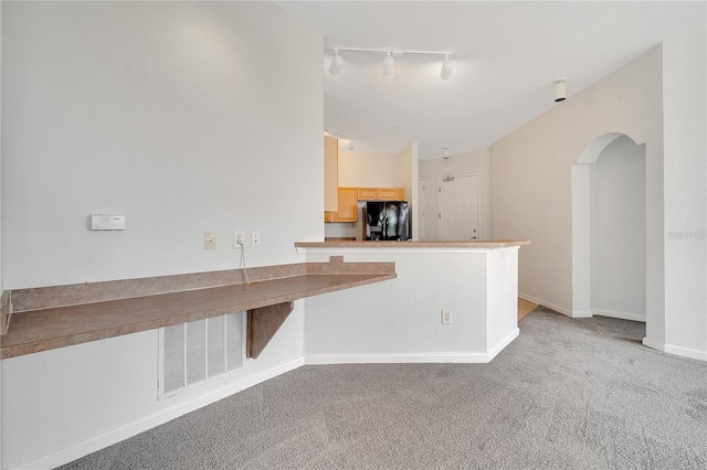 kitchen with light carpet, light brown cabinetry, black fridge, and track lighting