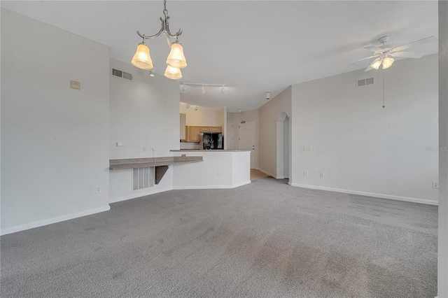 unfurnished living room with ceiling fan with notable chandelier, light colored carpet, and rail lighting