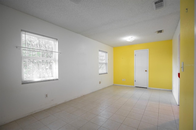 tiled empty room featuring a textured ceiling and a healthy amount of sunlight