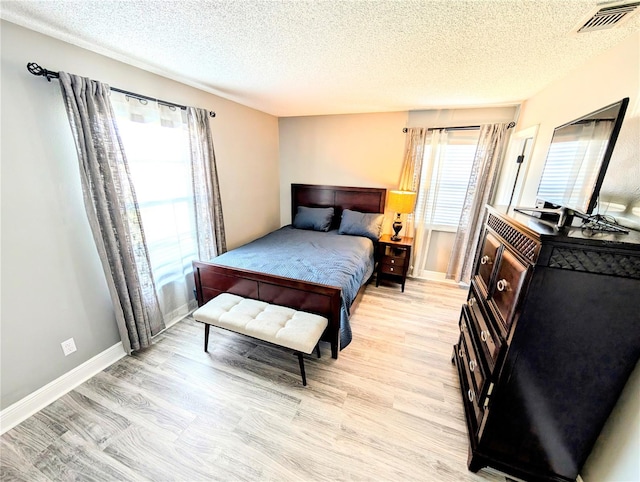 bedroom with a textured ceiling, multiple windows, and light hardwood / wood-style flooring