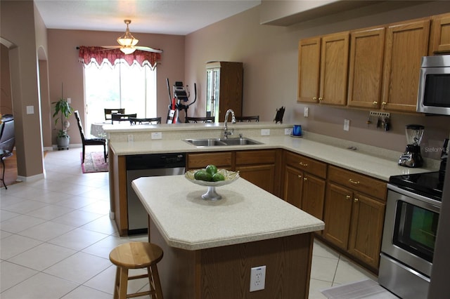 kitchen with light tile patterned floors, sink, kitchen peninsula, appliances with stainless steel finishes, and a center island