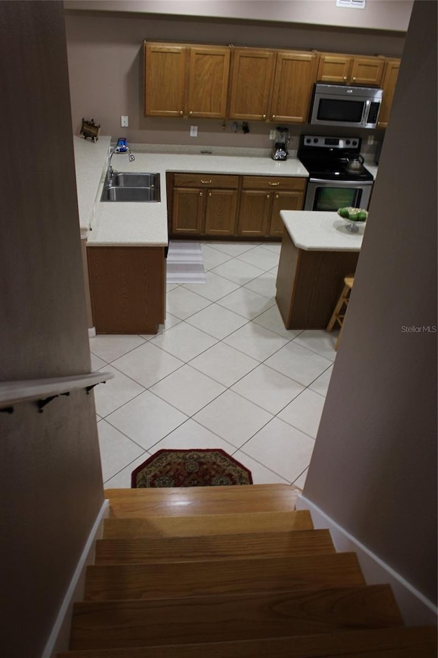 kitchen with stainless steel appliances, light tile patterned floors, sink, and a center island