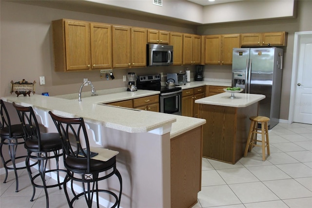 kitchen featuring kitchen peninsula, appliances with stainless steel finishes, a kitchen bar, and light tile patterned floors