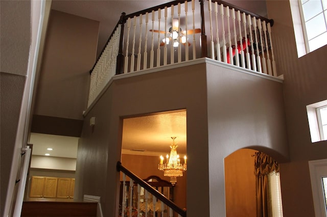 stairs featuring a towering ceiling, ornamental molding, and an inviting chandelier