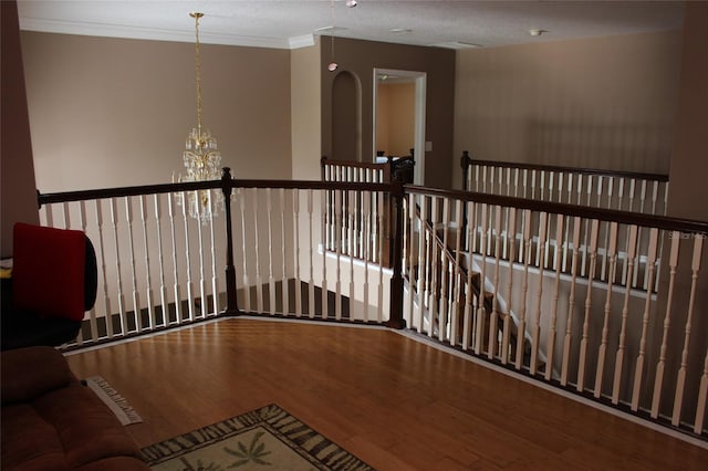 hallway with wood-type flooring, crown molding, an inviting chandelier, and a textured ceiling