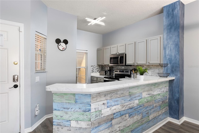 kitchen with gray cabinets, a textured ceiling, dark wood-type flooring, kitchen peninsula, and stainless steel appliances