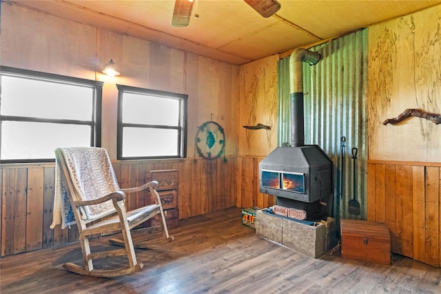 living area with ceiling fan, wood-type flooring, wooden ceiling, a wood stove, and wood walls