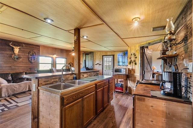 kitchen with sink, wood ceiling, wood walls, and an island with sink