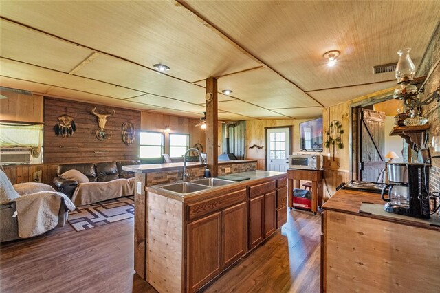 kitchen with dark hardwood / wood-style flooring, sink, a center island with sink, wooden ceiling, and wood walls