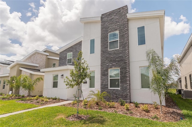 view of front of home featuring central AC, stone siding, a front lawn, and stucco siding