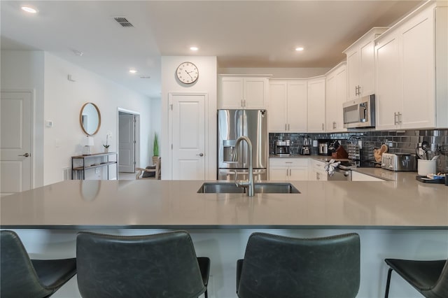 kitchen with a peninsula, visible vents, decorative backsplash, stainless steel appliances, and a sink