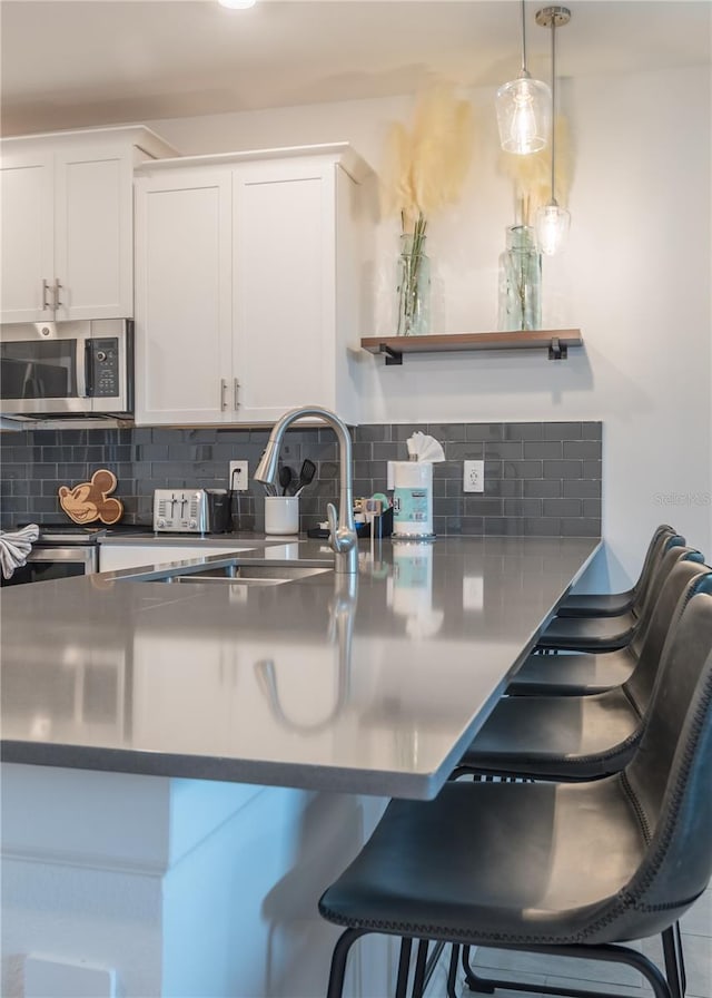 kitchen with stainless steel microwave, a breakfast bar, open shelves, white cabinets, and decorative backsplash