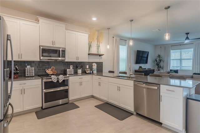 kitchen featuring a peninsula, open floor plan, decorative backsplash, stainless steel appliances, and a sink