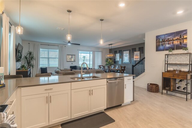 kitchen featuring pendant lighting, stainless steel dishwasher, white cabinets, a sink, and open floor plan