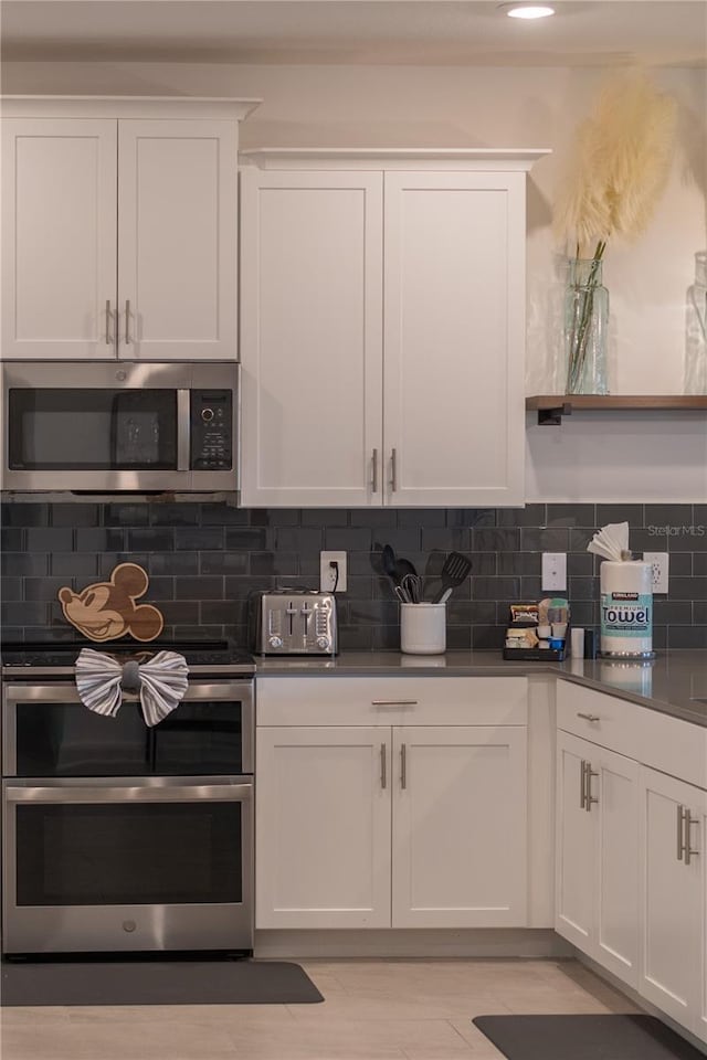 kitchen with white cabinets, dark countertops, decorative backsplash, and appliances with stainless steel finishes