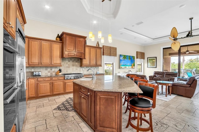 kitchen with light stone countertops, a breakfast bar area, stainless steel gas stovetop, a kitchen island with sink, and sink