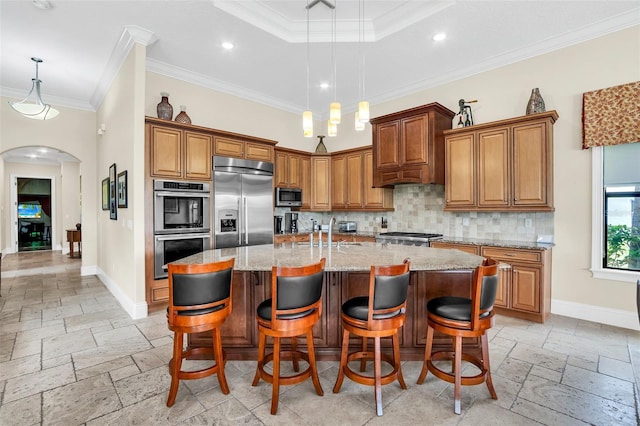 kitchen with an island with sink, light stone counters, appliances with stainless steel finishes, and crown molding