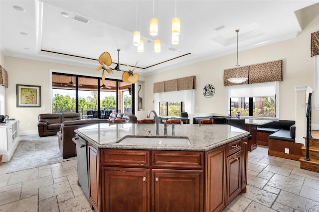 kitchen with light stone counters, sink, hanging light fixtures, a center island with sink, and crown molding