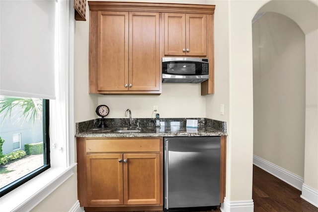 bar featuring dark stone countertops, appliances with stainless steel finishes, dark hardwood / wood-style floors, and sink