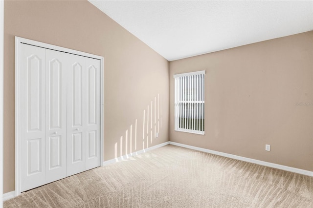 unfurnished bedroom featuring light colored carpet, a closet, and lofted ceiling