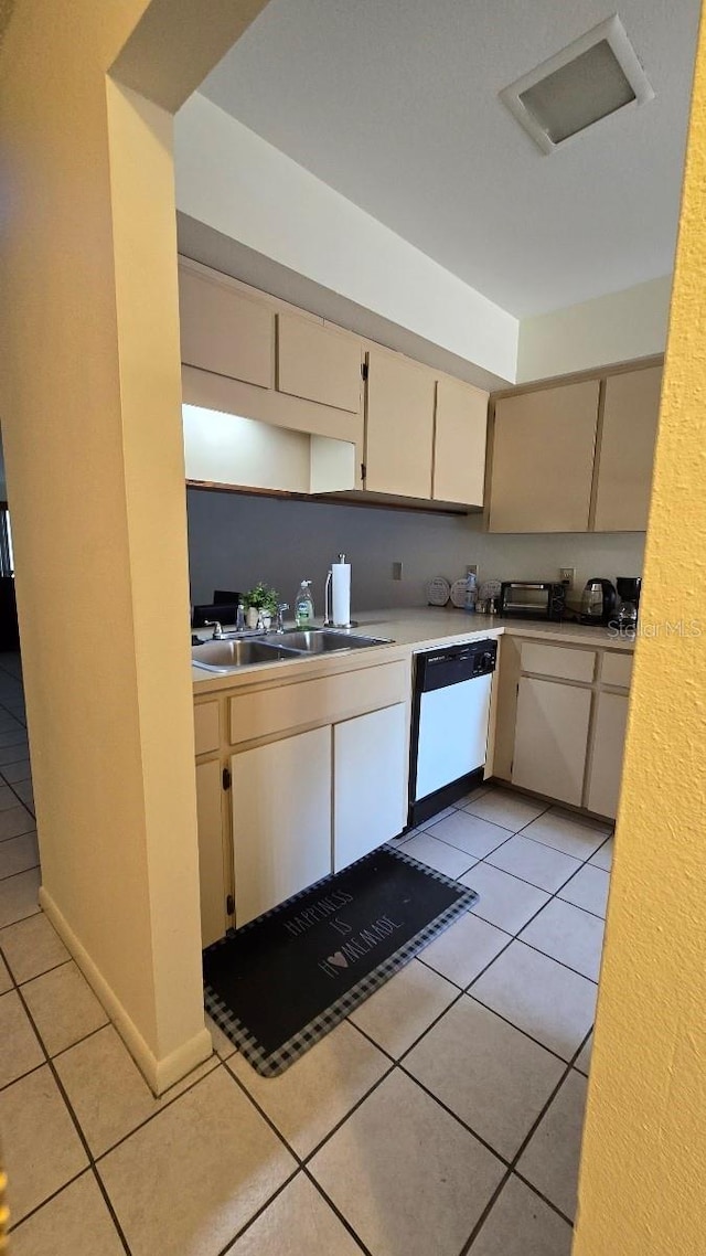 kitchen with white dishwasher, sink, light tile patterned flooring, and cream cabinets