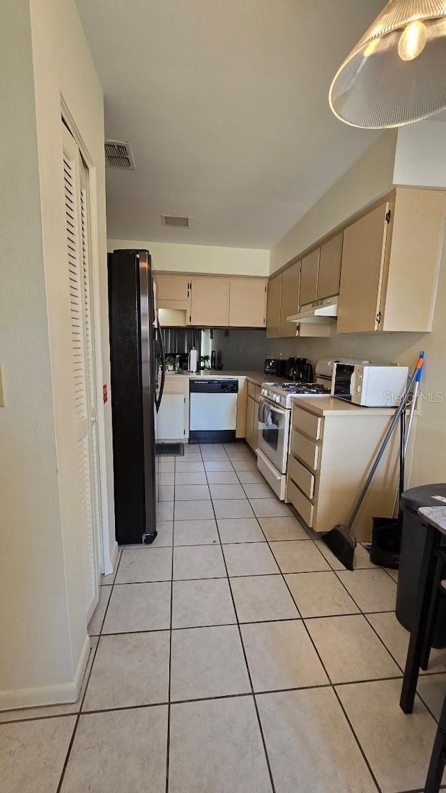 kitchen featuring cream cabinetry, light tile patterned floors, and white appliances