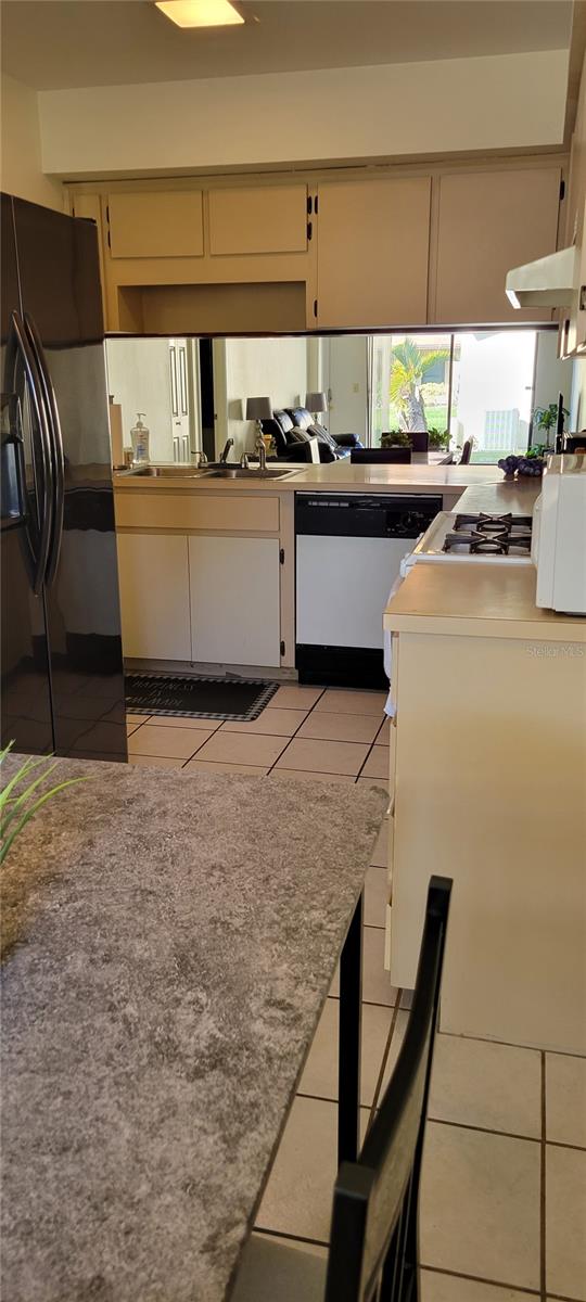 kitchen with black refrigerator with ice dispenser, light tile patterned floors, stainless steel gas stovetop, white dishwasher, and cream cabinetry