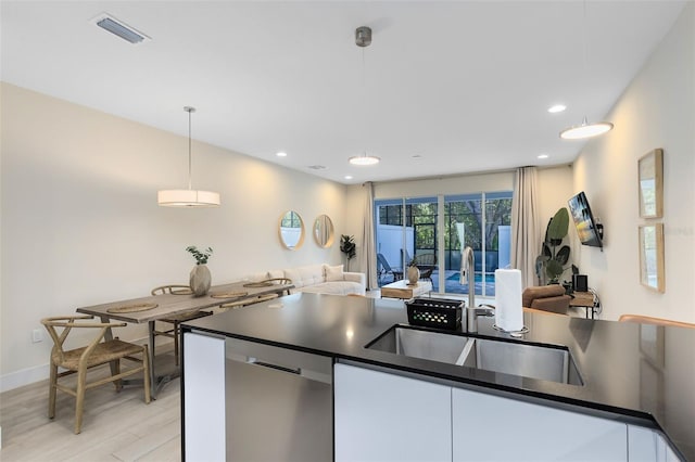 kitchen with light wood-type flooring, stainless steel dishwasher, white cabinetry, and decorative light fixtures