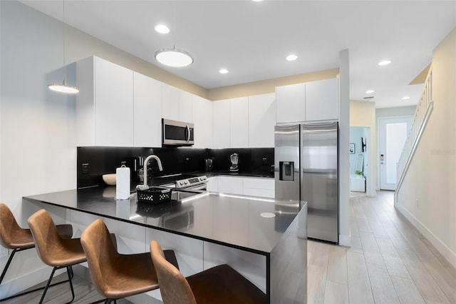 kitchen featuring white cabinets, hanging light fixtures, kitchen peninsula, stainless steel appliances, and a breakfast bar