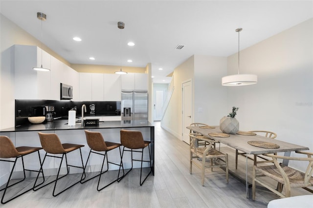 kitchen featuring light wood-type flooring, tasteful backsplash, white cabinets, hanging light fixtures, and appliances with stainless steel finishes